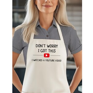 May include: Off-white apron with the text "DON'T WORRY I GOT THIS" above a red YouTube play button and the text "I WATCHED A YOUTUBE VIDEO". The apron has a neck loop and waist ties.