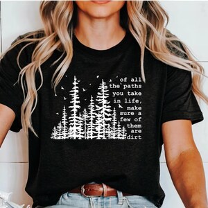May include: A black short-sleeved t-shirt featuring a white graphic print of a forest with pine trees and birds. The text reads: of all the paths you take in life, make sure a few of them are dirt. The shirt has a crew neckline and a straight hem.