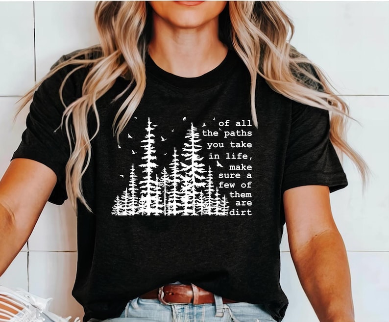 May include: A black short-sleeved t-shirt featuring a white graphic print of a forest with pine trees and birds. The text reads: of all the paths you take in life, make sure a few of them are dirt. The shirt has a crew neckline and a straight hem.