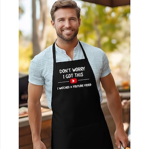 May include: Black apron with the text "DON'T WORRY I GOT THIS" above a YouTube logo and the text "I WATCHED A YOUTUBE VIDEO". The apron has a neck strap and waist ties.
