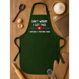 May include: A dark green apron with two front pockets and the text "DON'T WORRY I GOT THIS I WATCHED A YOUTUBE VIDEO" in white. The apron has a YouTube play button graphic. Kitchen tools and ingredients surround the apron.