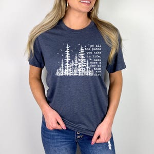 May include: A dark heather blue short-sleeve t-shirt featuring a white graphic of a forest with pine trees and birds. The text reads: of all the paths you take in life, make sure a few of them are dirt. The shirt has a crew neckline and a straight hem.
