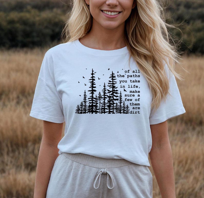 May include: A white short-sleeved t-shirt featuring a black graphic print of a forest silhouette with birds and the text: of all the paths you take in life, make sure a few of them are dirt. The shirt has a crew neckline and a relaxed fit.