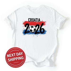 May include: White t-shirt with the word "CROATIA" above the number "2026" and a soccer ball graphic. The design incorporates red, white, and blue colors, resembling a flag. A red circle with the text "NEXT DAY SHIPPING" is at the bottom.