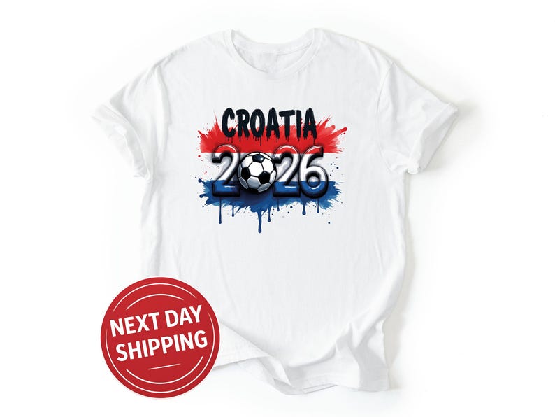 Puede incluir: Camiseta blanca con un dise&ntilde;o gr&aacute;fico que presenta la palabra "CROATIA" en negro, el n&uacute;mero "2026" y un bal&oacute;n de f&uacute;tbol. El dise&ntilde;o incorpora los colores rojo, blanco y azul, con un efecto de pintura goteando. Un c&iacute;rculo rojo con "NEXT DAY SHIPPING" est&aacute; en la parte inferior izquierda.