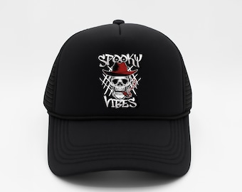 May include: Black trucker hat with a skull graphic wearing a red hat and smoking a cigarette. The words "Spooky Vibes" are above and below the skull. The hat has a mesh back and a curved brim.