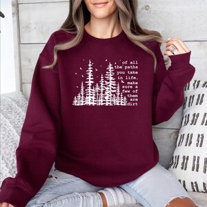 May include: A maroon long-sleeve crewneck sweatshirt featuring a white graphic of pine trees and birds. The text reads: of all the paths you take in life, make sure a few of them are dirt. The design is centered on the chest of the garment.