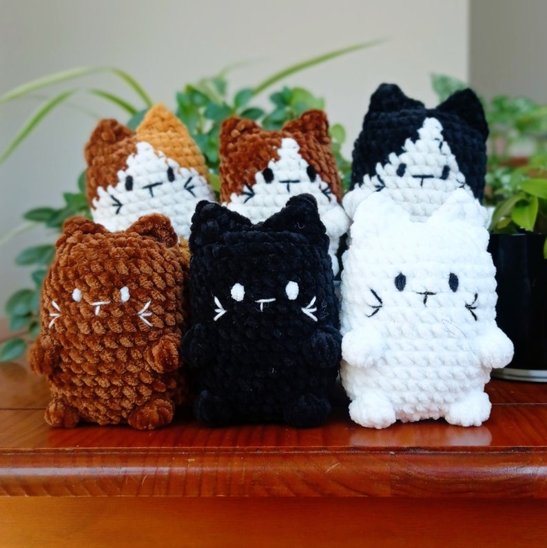Photo de six petits chat en peluche au crochet. Au premier plan de gauche à droite : un chat brun, un noir et un chat en peluche blanc. Au second plan : un chat calico puis beige/brun et enfin un chat en peluche au crochet noir/beige.