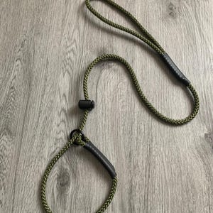 May include: Olive green dog leash with a loop handle and a sliding adjustment. The leash is made of a braided rope material and features black accents at the handle and the loop. The leash is designed for pet owners.
