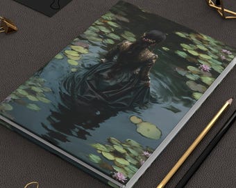 May include: A hardcover journal featuring a painting of a person in a dark dress in a pond with lily pads. Gold and black pencils and gold binder clips are on a dark gray surface.