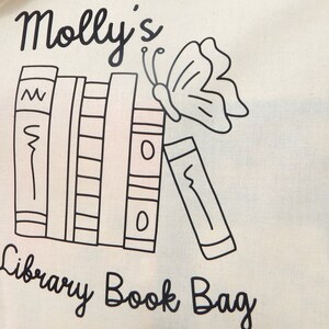May include: A white canvas tote bag with black text and a black and white illustration of a stack of books and a butterfly. The text on the bag reads "Molly's Library Book Bag".