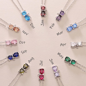 May include: Twelve silver necklaces with cat and butterfly charms, each with a different coloured gemstone. The necklaces are arranged in a circle with the months of the year written around them.