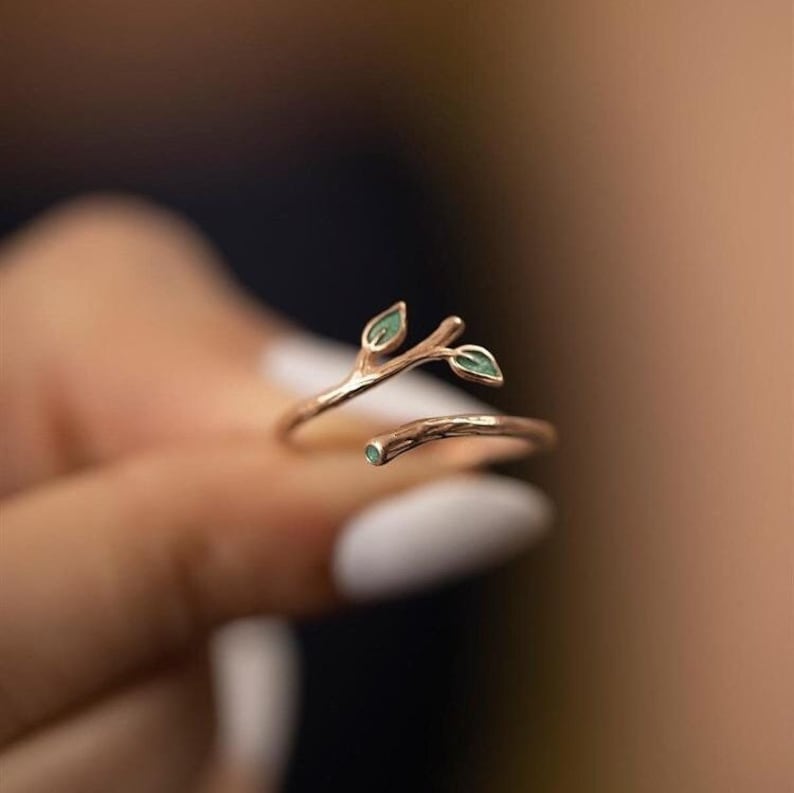 May include: A gold ring with a delicate twig design and two small green leaves. The ring is open and adjustable.