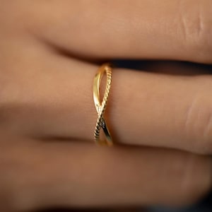 May include: A gold-toned ring with a twisted design. The ring is worn on a finger.