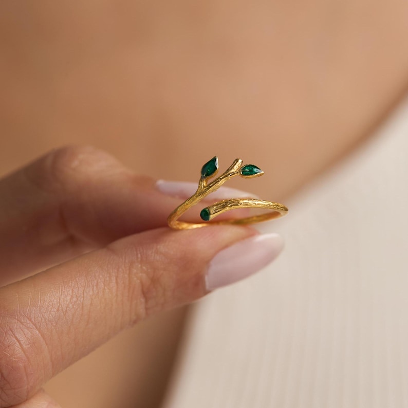 May include: Gold ring with a twig design and three green gemstones. The ring is open and adjustable.