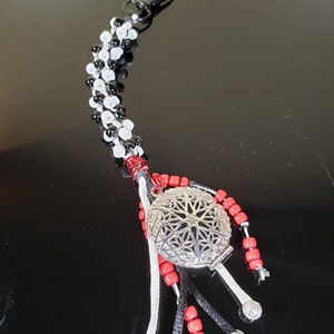 May include: A black and white beaded keychain with a silver charm and red beads. The charm has a filigree design and is attached to a black cord with red beads. The keychain has a silver clip.