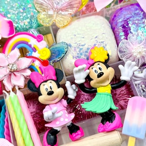 May include: A clear plastic storage box filled with colorful craft supplies, including a rainbow, a butterfly, glitter, and two small Minnie Mouse figurines. One Minnie Mouse is wearing a pink dress with white polka dots, and the other is wearing a green hula skirt.