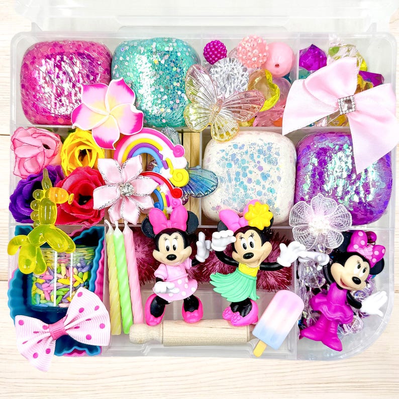 May include: A clear plastic storage container filled with colorful play dough, toys, and accessories. The container has multiple compartments and includes a variety of items, such as glitter, flowers, bows, candles, and figurines.