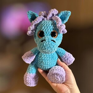 May include: A crocheted blue and purple unicorn plush toy with large brown eyes.
