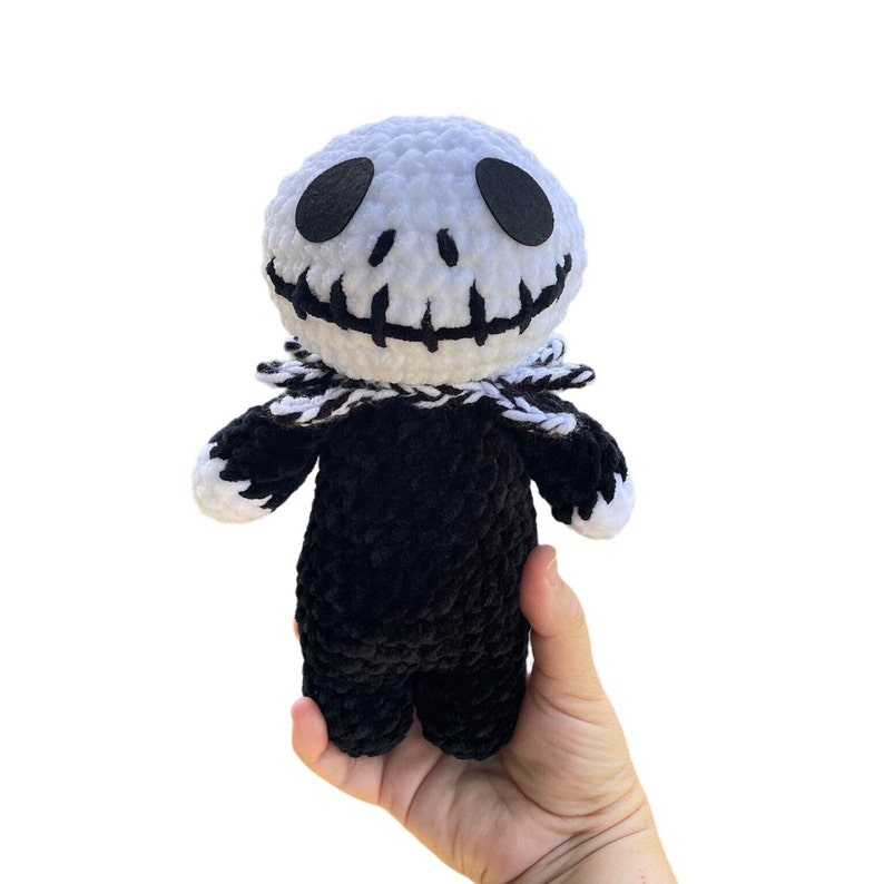 May include: A crocheted plush toy of Jack Skellington from the Nightmare Before Christmas. The toy is white with black eyes and a black stitched smile. The body is black and the collar is white and black.