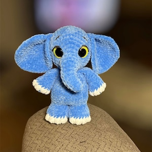 May include: A blue crocheted elephant plush toy with white accents and yellow eyes.