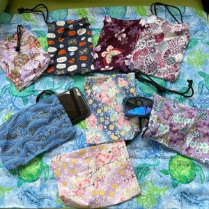 May include: Assortment of small drawstring bags with various floral and geometric patterns. The bags are made of fabric and have a variety of colors, including blue, purple, pink, and red. A cell phone and sunglasses are also pictured.