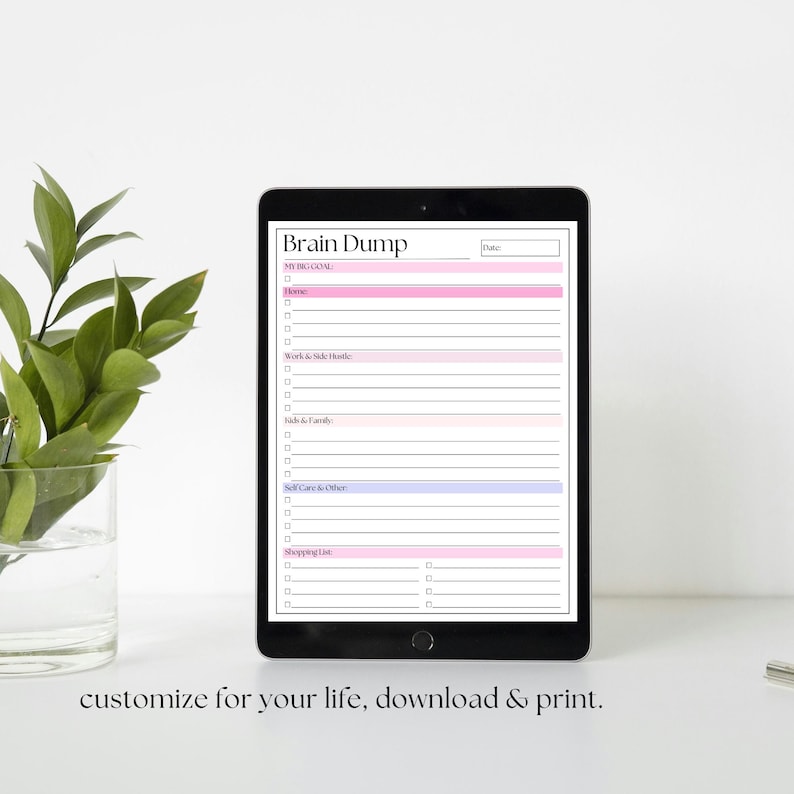 Op de afbeelding: Een zwarte tablet toont een "Brain Dump" sjabloon met roze en blauwe secties voor doelen, thuis, werk, familie, zelfzorg en winkelen. De tekst "customize for your life, download & print" staat onderaan.