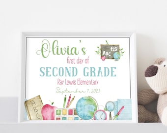 May include: A white framed sign featuring the text Olivia's first day of SECOND GRADE Ray Lewis Elementary September 7, 2023. The design includes watercolor illustrations of a chalkboard, an apple, pencils, a paint set, a globe, and a clock.