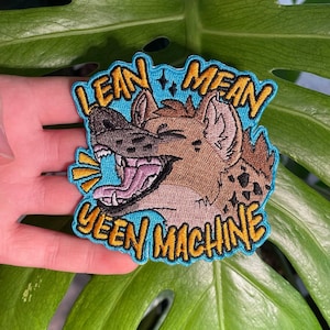May include: Embroidered patch with a cartoon hyena design. The patch has a blue background with the words "LEAN MEAN YEEN MACHINE" in yellow, outlined in black. The hyena is brown, tan, and black. The patch is likely for clothing.