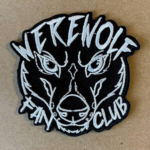 Puede incluir: Parche bordado en blanco y negro con una cabeza de hombre lobo y el texto "WEREWOLF FAN CLUB".