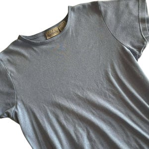 May include: A light blue short-sleeved t-shirt. The shirt has a crew neck and a small tag on the neckline. The fabric appears soft and slightly textured. The shirt is a solid color and has a simple, classic design.