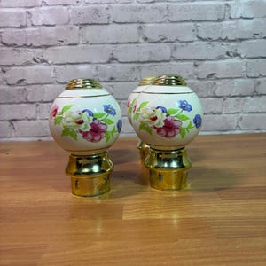 May include: Set of four decorative curtain rod finials. Each finial features a cream-colored, spherical design with a gold band and base. The spheres are adorned with floral patterns in pink, white, and blue, adding a touch of elegance to any window treatment.