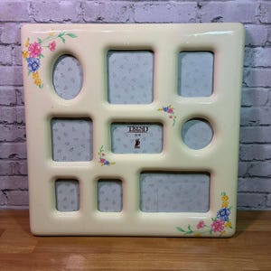 May include: Cream-colored multi-photo frame with various sized openings. Floral accents in pink, blue, and yellow adorn the corners. The frame has a glossy finish and includes the text "TREND" in the center.