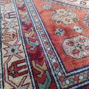 May include: Close-up of a red, blue, and beige patterned rug with intricate designs. The rug has a traditional style and features a central medallion with geometric shapes.