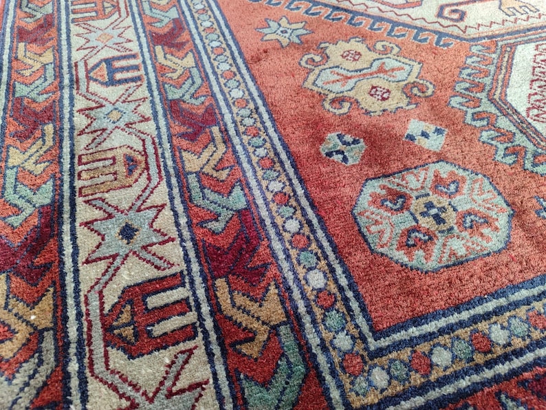 May include: Close-up of a red, blue, and beige patterned rug with intricate designs. The rug has a traditional style and features a central medallion with geometric shapes.