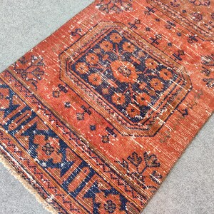 K&ouml;nnte beinhalten: Ein Vintage-Teppich mit einem roten und blauen geometrischen Muster. Der Teppich hat einen Fransenrand und ist aus Wolle.