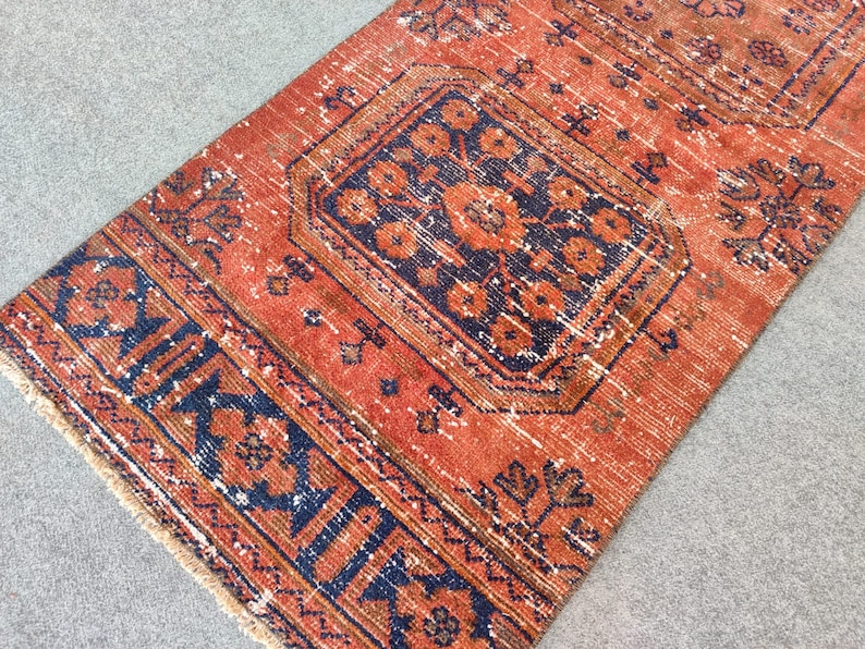 K&ouml;nnte beinhalten: Ein Vintage-Teppich mit einem roten und blauen geometrischen Muster. Der Teppich hat einen Fransenrand und ist aus Wolle.