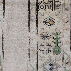 Puede incluir: Primer plano de una alfombra beige con un patr&oacute;n geom&eacute;trico en tonos de verde, marr&oacute;n y azul. La alfombra tiene un borde con flecos.