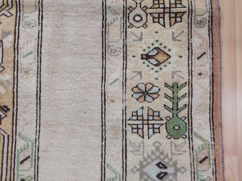 Puede incluir: Primer plano de una alfombra beige con un patr&oacute;n geom&eacute;trico en tonos de verde, marr&oacute;n y azul. La alfombra tiene un borde con flecos.