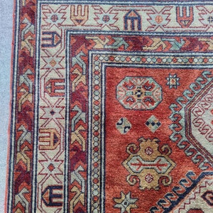 May include: Close-up of a red, blue, and beige patterned rug with intricate geometric designs. The rug has a fringe border.