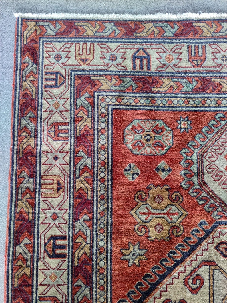 May include: Close-up of a red, blue, and beige patterned rug with intricate geometric designs. The rug has a fringe border.