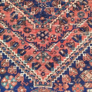 May include: A close-up of a red, blue and white patterned rug with a geometric design. The rug has a traditional Persian style.