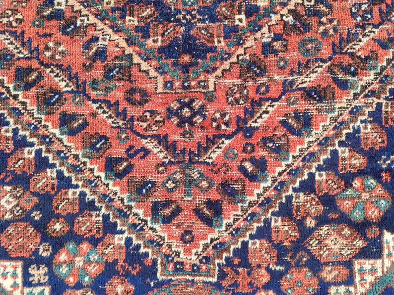 May include: A close-up of a red, blue and white patterned rug with a geometric design. The rug has a traditional Persian style.