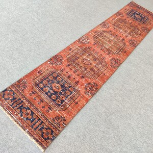K&ouml;nnte beinhalten: Ein langer, rechteckiger Teppich mit traditionellem persischem Design. Der Teppich ist rot mit blauen und wei&szlig;en Akzenten. Der Teppich hat ein Blumenmuster und einen geometrischen Rand.