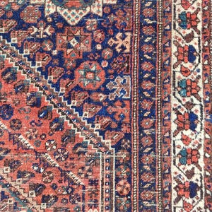 May include: A vintage rug with a red, blue and white geometric pattern. The rug has a fringed border and is made of wool.