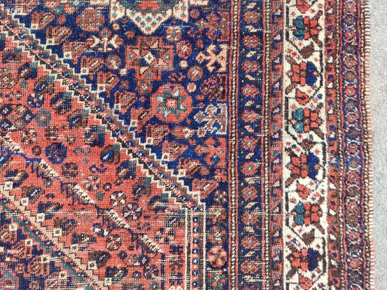 May include: A vintage rug with a red, blue and white geometric pattern. The rug has a fringed border and is made of wool.