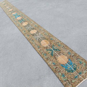 Könnte beinhalten: Ein langer, schmaler Teppich mit traditionellem persischem Design. Der Teppich ist hauptsächlich braun mit Akzenten in Blau, Grün und Beige. Der Teppich hat an beiden Enden Fransen.