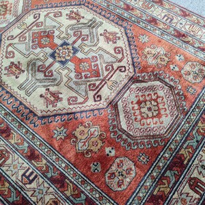 May include: A traditional rug with a red, beige, and blue geometric pattern. The rug has a central medallion with a repeating design of stylized flowers and leaves.