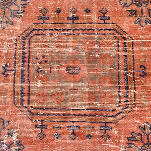 K&ouml;nnte beinhalten: Ein Vintage-Teppich mit rotem Hintergrund und einem zentralen Medaillon in einem dunkleren Rotton. Der Teppich hat ein geometrisches Muster mit komplizierten Details in Blau und Braun.