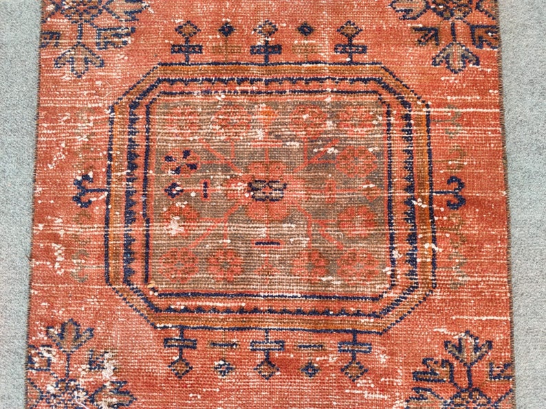 K&ouml;nnte beinhalten: Ein Vintage-Teppich mit rotem Hintergrund und einem zentralen Medaillon in einem dunkleren Rotton. Der Teppich hat ein geometrisches Muster mit komplizierten Details in Blau und Braun.